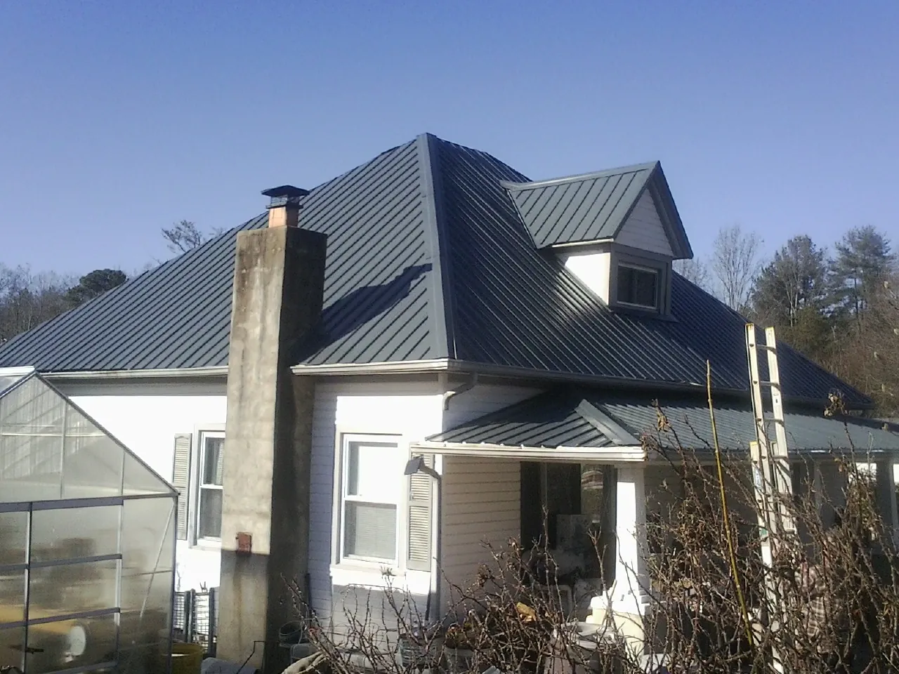 Dark blue standing seam metal roof on a white farmhouse with dormer — Slate & Tile Roof Repair by Roofing Brothers in Harveyville