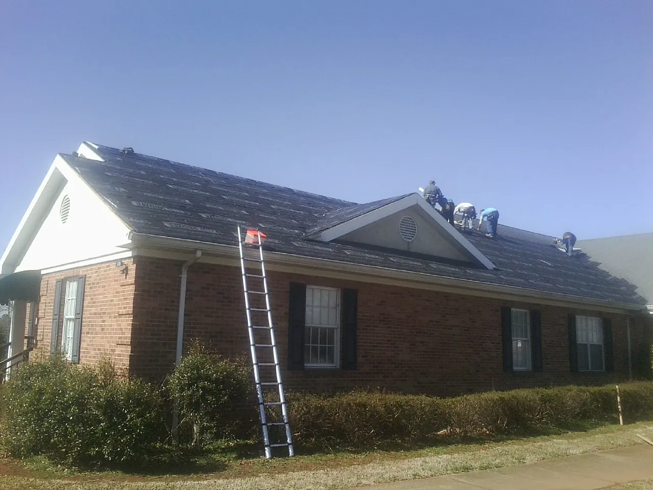 Crew tearing shingles off a brick ranch roof with a ladder set — Metal Roof Repair work by our crew in Harveyville