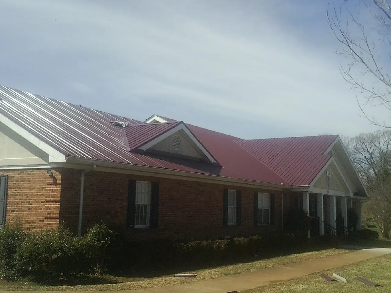 Red metal roof with gabled entries on a long brick building, from a Hail Damage Roof Repair job in Harveyville