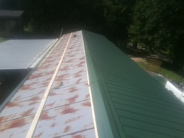 Old rusted panels beside newly installed green metal roofing — Wind Damage Roof Repair by Roofing Brothers in Harveyville