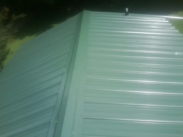 New green metal panels meeting at the ridge of a roof — Flat Roof Repair work by our crew in Harveyville