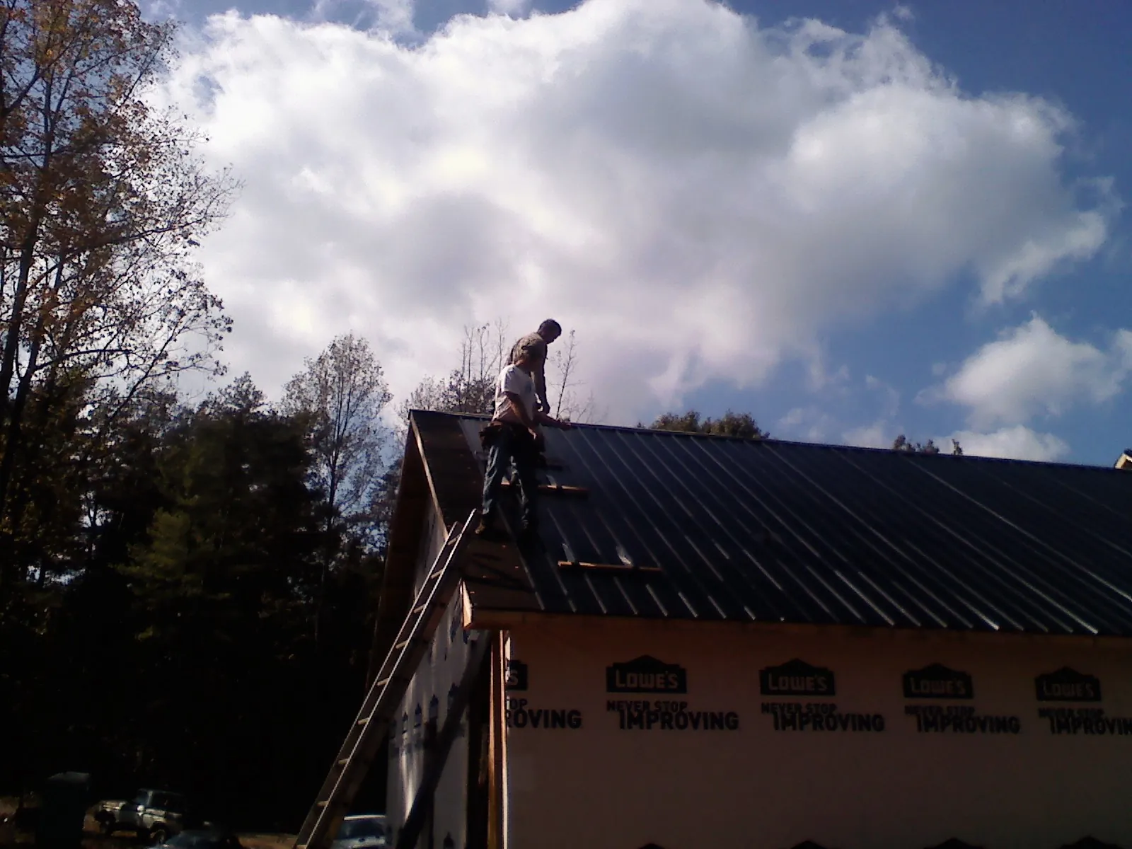 Roofer fastening dark metal panels high against a cloudy sky, from a Roof Inspection job in Harveyville