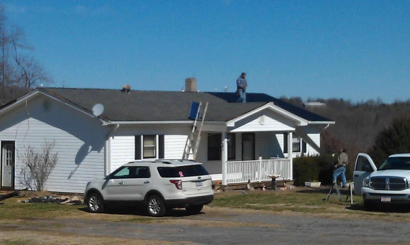 Roofers stripping shingles from a white ranch house roof in Harveyville