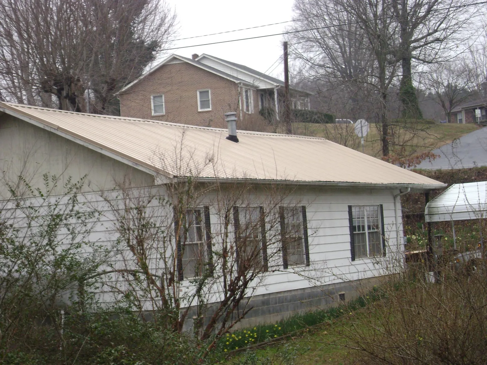 Tan metal roof on a white sided house set into a hillside — Commercial Roofing by Roofing Brothers in Harveyville