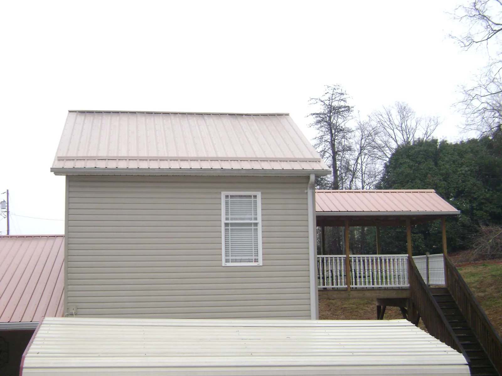 Tan metal roofs on a two story addition and attached porch, from a Roof Replacement job in Harveyville